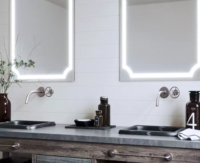 Double Belfast sinks with wall-hung lighted mirrors in a modern washroom.