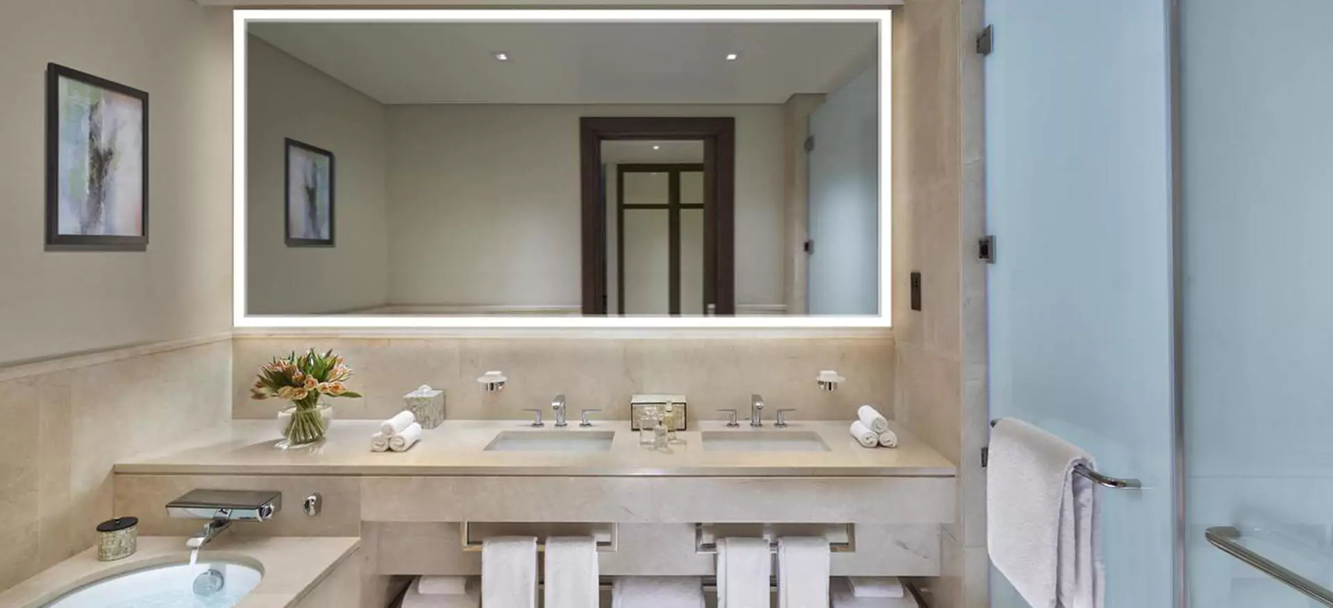 Light-framed mirror embedded in a wall of a bathroom basin.