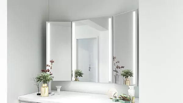 An icon of a trifold-lighted mirror set on a white wall above a cabinet with a round stool.