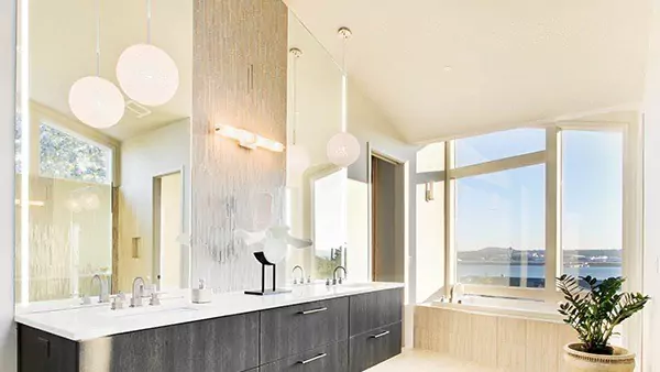 A thumb of a lit mirror is set on a white wall above a black bathroom cabinet with a sink.