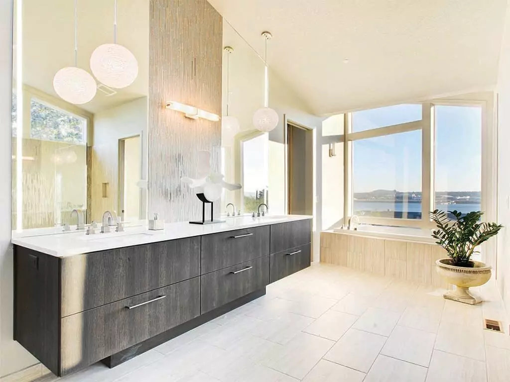 An extended, lighted mirror is set on a white wall above a black bathroom cabinet with a sink.