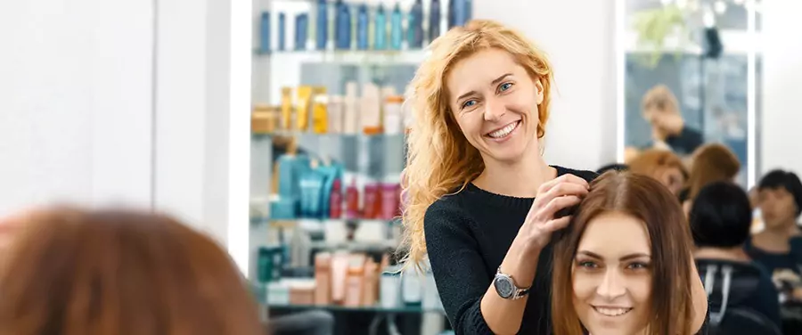 Reflection of a joyful female while holding the hair of a woman's customer in a mirror.