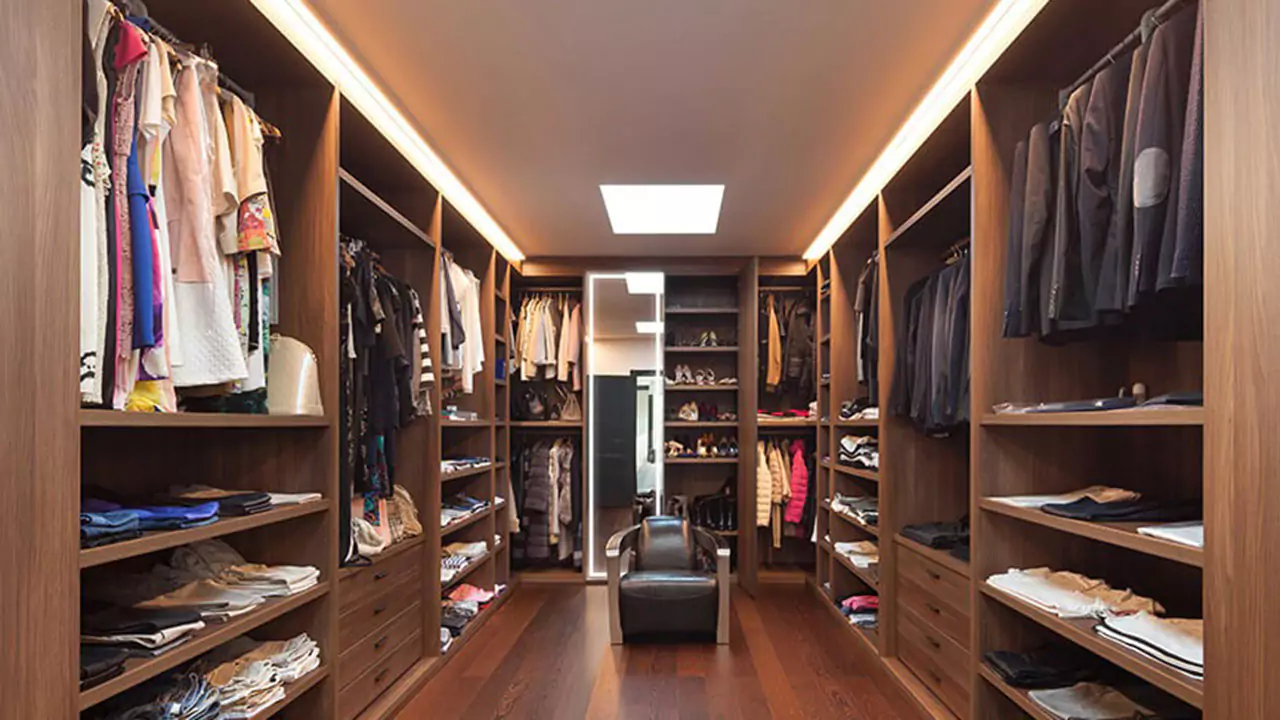 Walk-in wooden closet with a lighted mirror and a leather chrome aviator lounge chair.